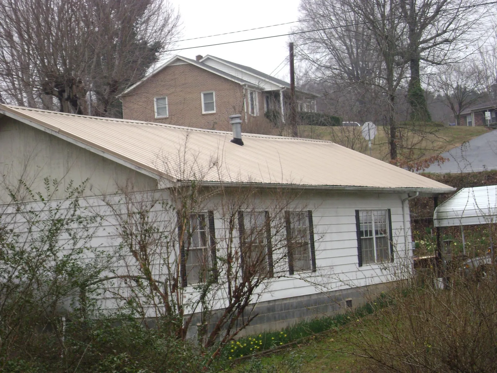 Tan metal roof on a white sided house set into a hillside — Commercial Roofing by Roofing Brothers in Portland