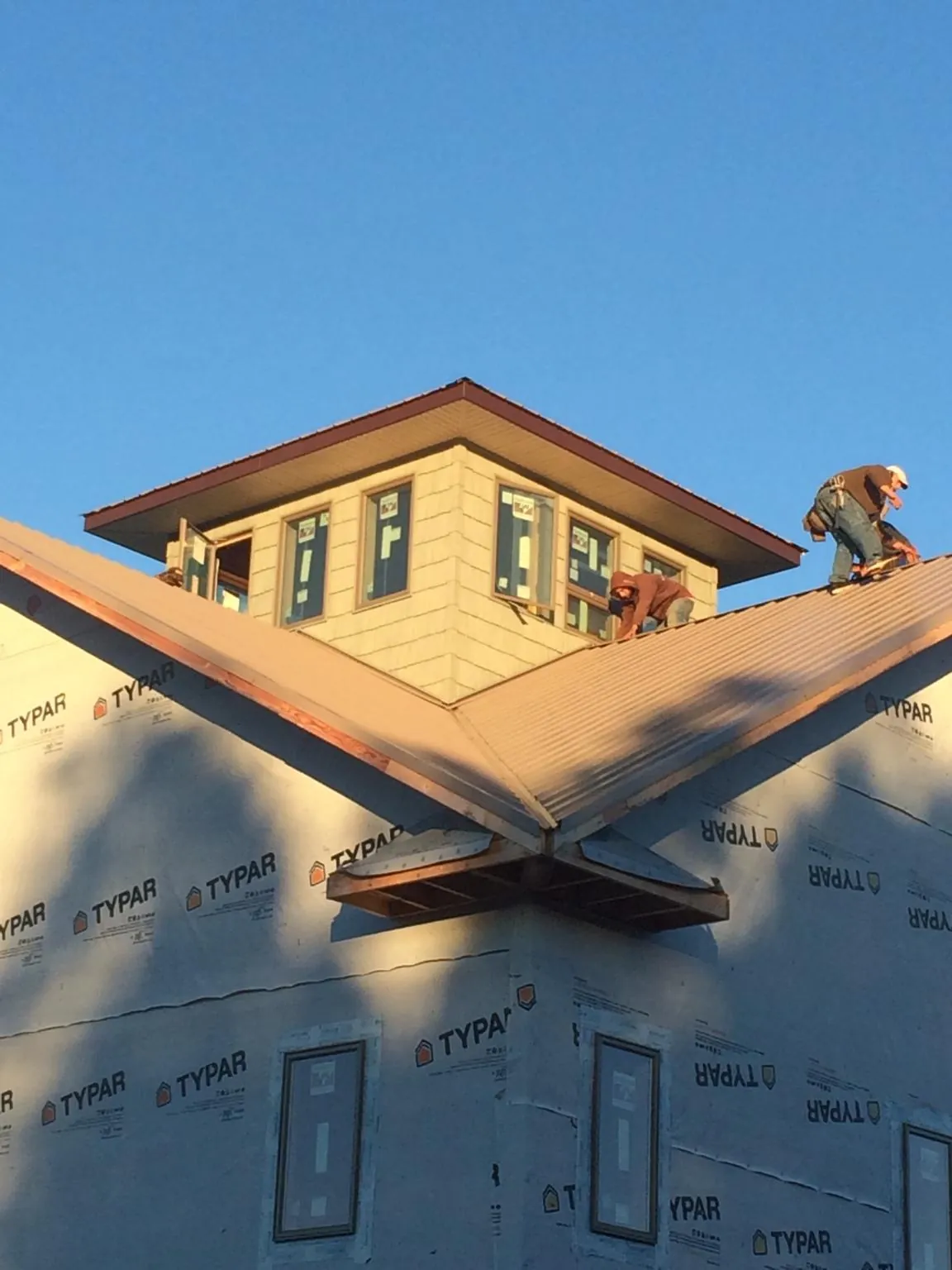 Roofers working around a rooftop cupola on a new metal roof at sunset in Portland